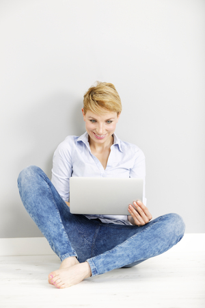 Attractive young woman using her laptop computer sitting on the floorの写真素材