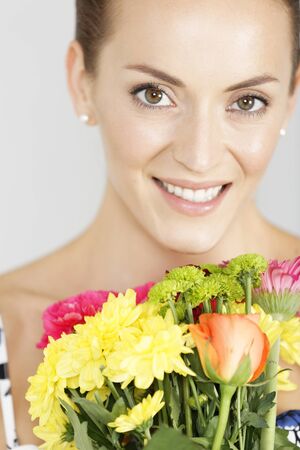 Beautiful young woman in a summer dress holding a fresh bouquet of flowers smilingの写真素材