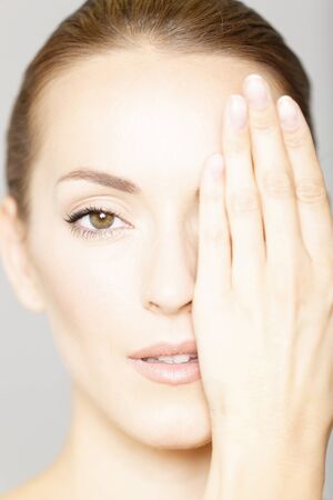 Beautiful young woman with her hand covering part of her face in a beauty style poseの写真素材