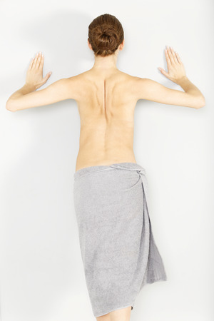 Attractive young woman topless leaning against a wall stretchingの写真素材