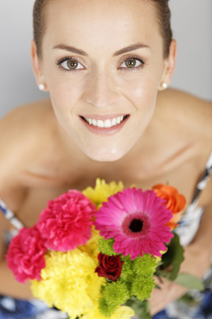 Beautiful young woman in a summer dress holding a fresh bouquet of flowers smilingの写真素材