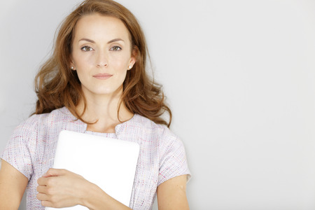 Young woman holding a closed laptop waiting for an appointment in a smart purple dressの写真素材