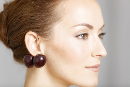 Attractive young woman wearing cherries as ear ringsの写真素材