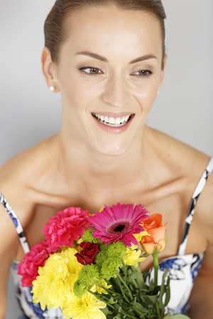 Beautiful young woman in a summer dress holding a fresh bouquet of flowers smilingの写真素材