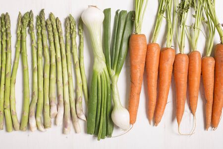 fresh raw asparagus on a light wooden kitchen work surface with carrots and spring onionsの写真素材