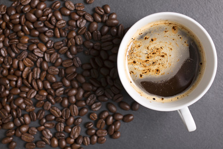 Still life of fresh roasted coffee beans with a white mug on a black slate surfaceの写真素材