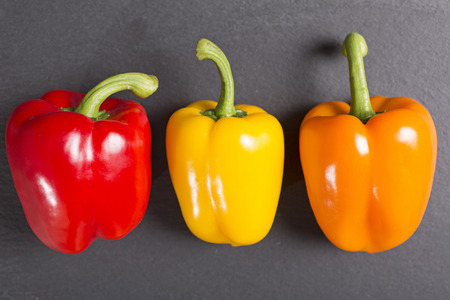 Fresh selection of ripe red yellow and orange peppers on black slateの写真素材