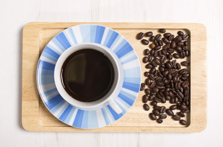 Fresh cup of coffee with roasted beans scattered around on a serving trayの写真素材