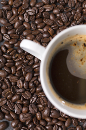 Still life of fresh roasted coffee beans with a white mug on a black slate surfaceの写真素材