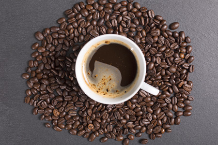 Still life of fresh roasted coffee beans with a white mug on a black slate surfaceの写真素材