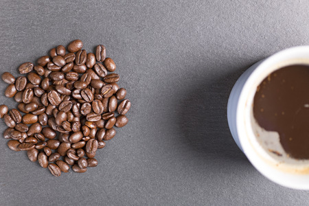 Still life of fresh roasted coffee beans with a white mug on a black slate surfaceの写真素材