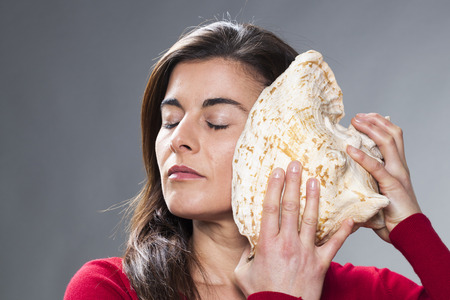 young brunette woman listening to the ocean sound from a giant shell