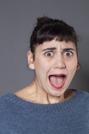 fear concept - portrait of terrified 20s woman with blue winter sweater screaming out,mouth wide open ,studio shotの写真素材