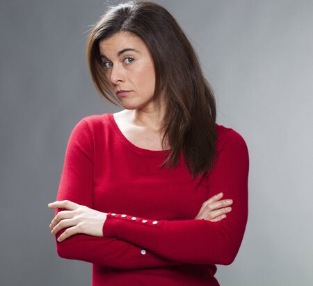 interrogative young woman with brown hair and red sweater with arms folded,turning head for...