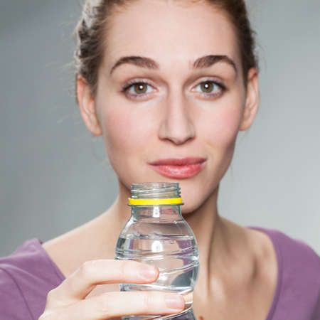 focus on hand holding a bottle of water with a radiant young beautiful woman in background