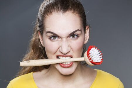 young gorgeous woman biting dish brush for housekeeping rebellion and strong disagreementの写真素材