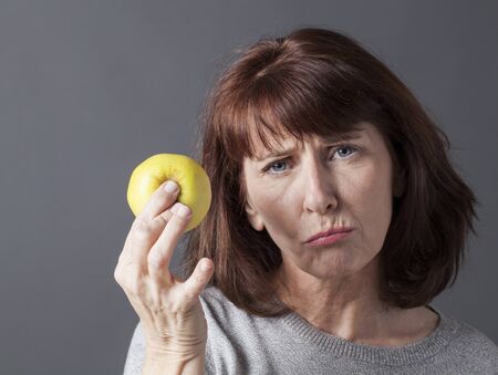 unhappy mature woman holding yellow golden apple in hand for vitamins dietの写真素材