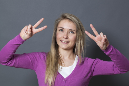 success concept - happy young blonde girl showing a double victory sign for achievementの写真素材
