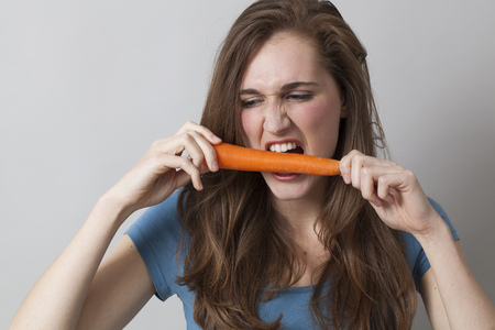 young beautiful woman biting carrot with anger for frustrating dietの写真素材