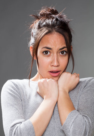 fear concept - scared mixed race 20s woman with brown hair protecting herself with both hands on shoulders,studio shotの写真素材
