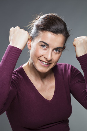 success concept - beautiful young woman showing her muscles expressing her happiness and power with tensed fists up and tightの写真素材