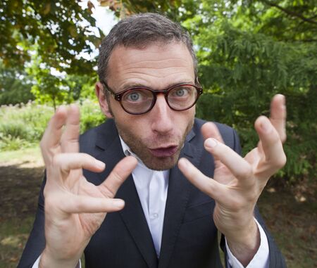 mad scientist outdoor concept - crazy businessman showing his mad face and strange hands in foreground in green environment for corporate involvement,natural summer daylightの写真素材