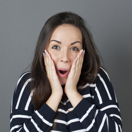 surprise and success concept - cheerful 20s woman putting both hands on her face smiling for surprise and happinessの写真素材