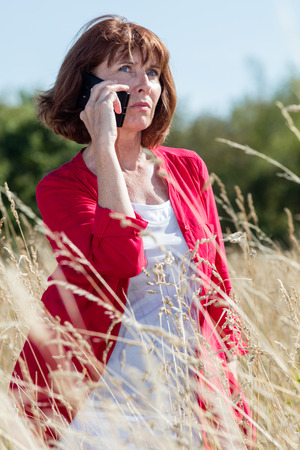 outdoors communications - thinking senior woman talking on the phone alone in long dry grass field to be quiet,blue sky,natural summer daylightの写真素材