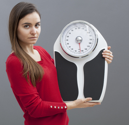 confident young woman with weighting scale in hands for concept of weight loss or weight controlの写真素材