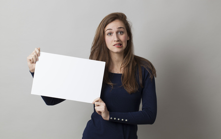 stunned young woman biting her lips in holding a scary news on a blank bannerの写真素材
