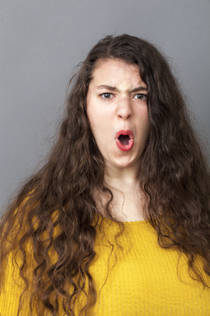 angry overweight 20's woman with long brown hair screaming loud for expressing rage and impatienceの写真素材