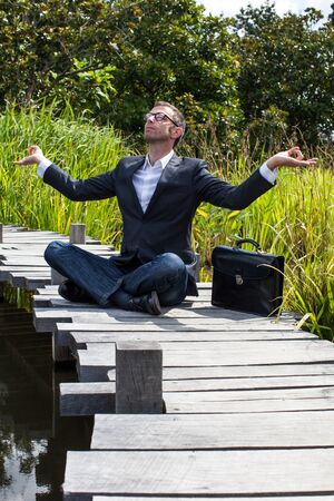 corporate green break - zen middle age male professional sitting on a wooden path in the middle of an asian-like green pond for company wellnessの写真素材
