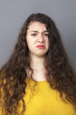 unhappiness and disappointment concept - frowning young overweight woman with long brown hair expressing disgust and dislike with a funny face,studio shotの写真素材
