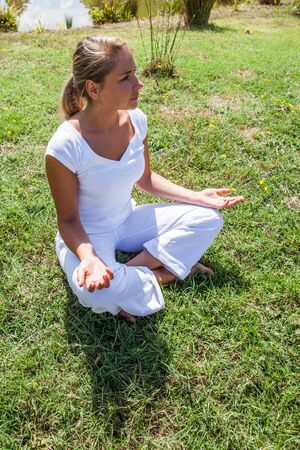 outdoors zen exercise - smiling young yoga woman escaping in relaxing in lotus pose on the grass, summer daylight, high angle viewの写真素材