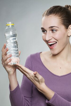 thrilled young beautiful woman wearing purple shirt showing bottle of citrus mineral water