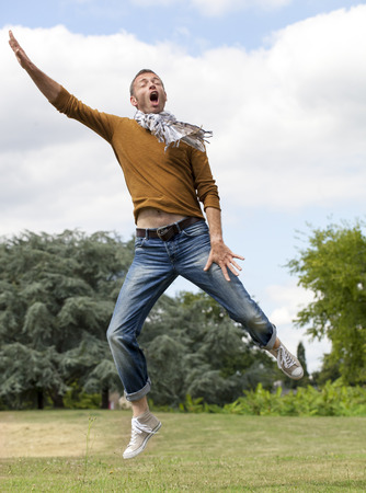 celebrating success outdoors concept - dynamic modern man jumping with arms raised with energy for freedom and happiness in green park,natural summer daylightの写真素材