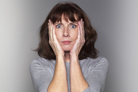 portrait of anxious beautiful 50's woman under shock with both hands on face for fear and stressの写真素材