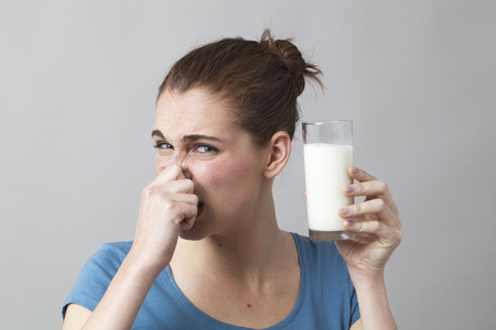 young woman not willing to drink a glass of smelly milk or disgusting white beverageの写真素材