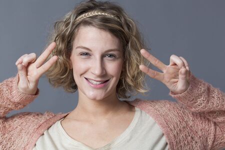 satisfaction concept - thrilled young woman with curly blonde hair making a double sign of victory for agreementの写真素材