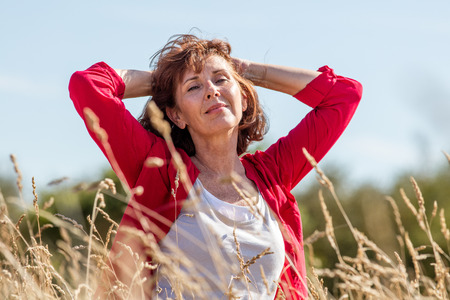 female casual relaxation - smiling radiant mature woman enjoying fresh air in her hair,being in harmony with nature in long summer grass field seeking for peace,summer daylightの写真素材