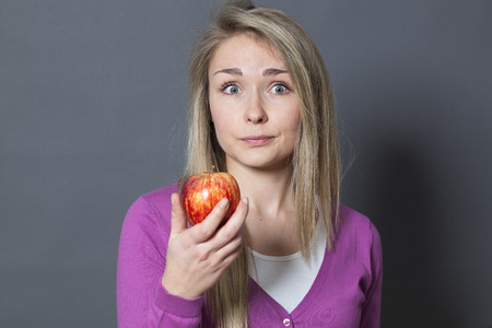 thinking young blonde woman with a red apple on her hands acting surprisedの写真素材
