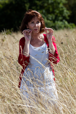 loneliness in countryside - beautiful 50s woman in reflection alone in long dry field or meadow,natural summer daylightの写真素材