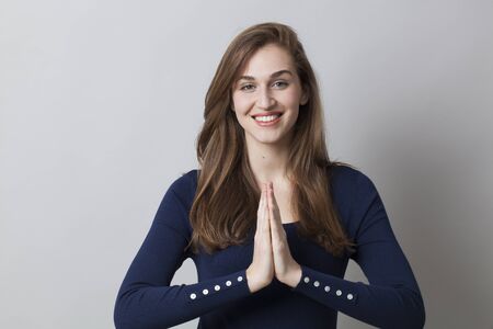 happiness and calm concept - zen smiling young woman wearing a smart navy blue sweater holding hands together for relaxationの写真素材
