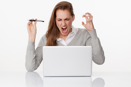 trouble at work concept - furious young female student or office worker working on computer and internet,studio shot,white backgroundの写真素材