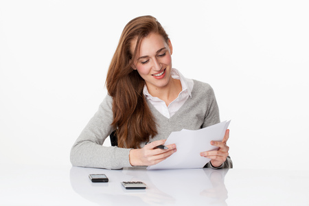 satisfaction at work concept - smart young woman smiling in looking at her sales figures, studying accounting at her desk,studio shot,modern white backgroundの写真素材