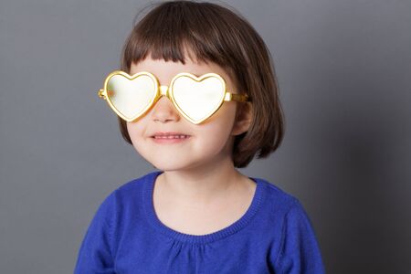 fun kid glasses concept - bright preschool child wearing dazzling yellow heart-shape glasses for positive future,studio shotの写真素材