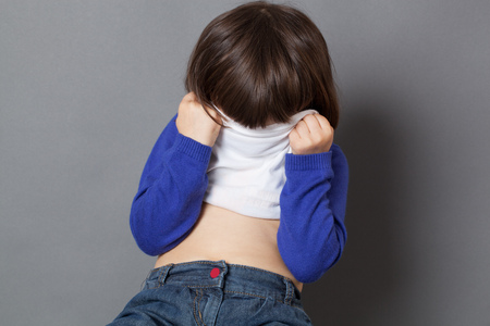 kid fun concept - shy preschool child playing peekaboo or hide and seek behind sweater to be invisible at school,studio shotの写真素材