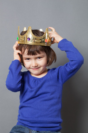 spoiled kid concept - lovely 4-year old child putting a crooked golden crown on head for mollycoddled little king or queen metaphor,studio shotの写真素材