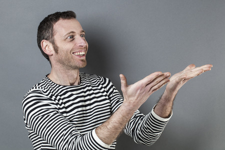 body language concept - thrilled 40s man smiling in showing a product or advertisement with cheerful hand gesture,studio shot on gray backgroundの写真素材