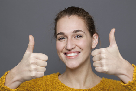 radiant approval concept - gorgeous 20s girl smiling with double thumbs up for satisfaction and success,studio shot on gray backgroundの写真素材